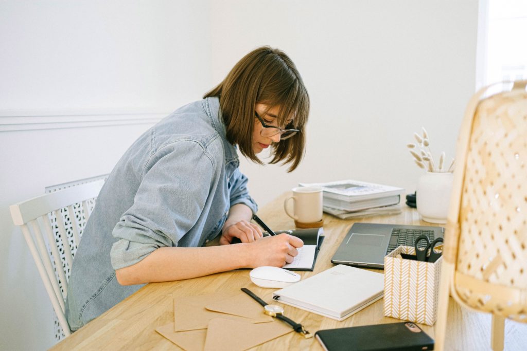 Frau schreibt in ein Notizbuch an einem Schreibtisch